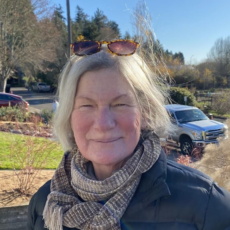 Outdoor portrait of an older woman with grey hair and sunglasses on head with a black puffy jacket and scarf.